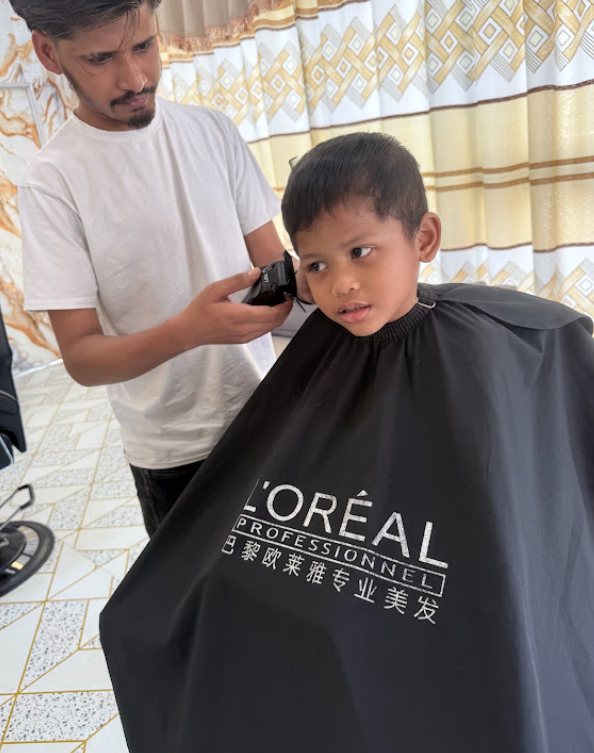 Barber giving a child a haircut at Newaj Barber Shop Setia Alam